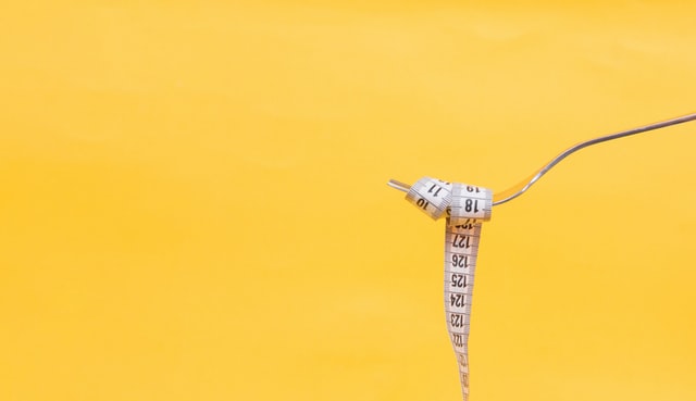tape measure wrapped around fork against yellow background