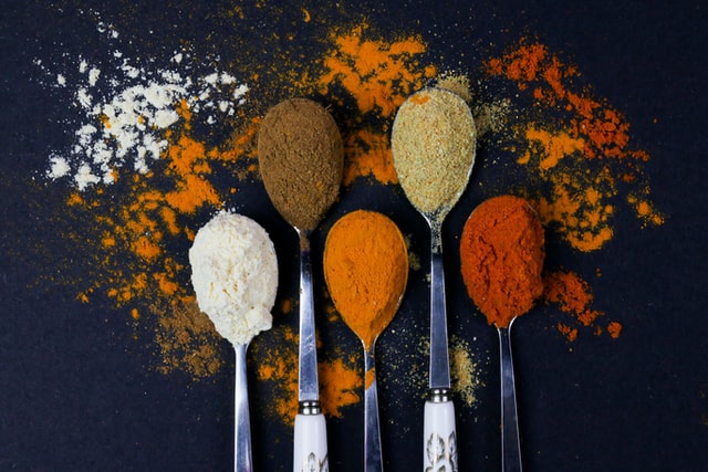 5 spoons with differently colored spices against dark background