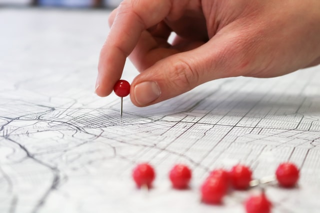 close-up of hand placing red pins on a map (geography concept)